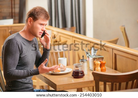 Could you bring some more coffee. Handsome young man calling a waiter in cafe while sitting at the table and raising his hand above the head