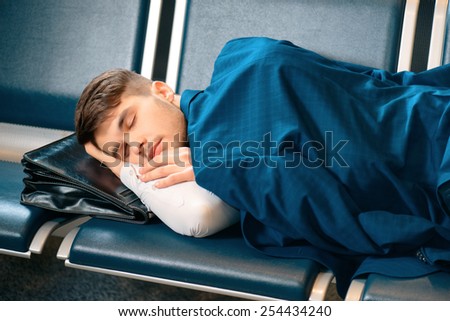 Tired and overworked. Exhausted business man in formalwear sleeping on the rows of chairs in the hall of the airport covering his shoulders with a jacket
