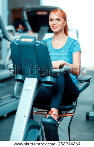 Cycling on exercise bike. Beautiful mature woman in sports clothing training on exercise bicycle in the gym
