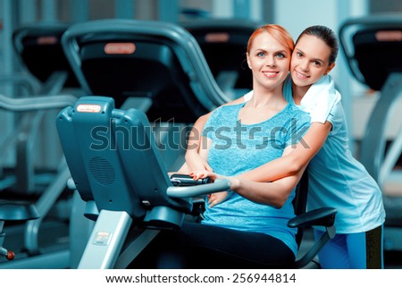 Training with mom. Beautiful mature woman bonding her teenage daughter in sports clothing after workout on exercise bicycle in the gym