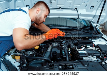 Best mechanic around. Handsome muscular car mechanic in uniform checking the engine in car service station