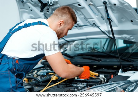 Passionate about cars. Handsome muscular car mechanic in uniform checking the engine in car service station