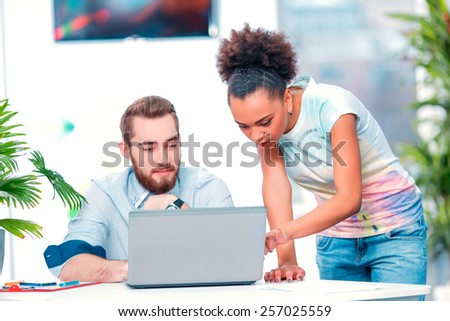 Creative team at work. Young African woman and Caucasian man in smart casual looking at laptop together while sitting in creative space