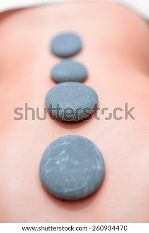 Stone SPA. Top view of young woman with shiny skin lying on front with spa stones on her back