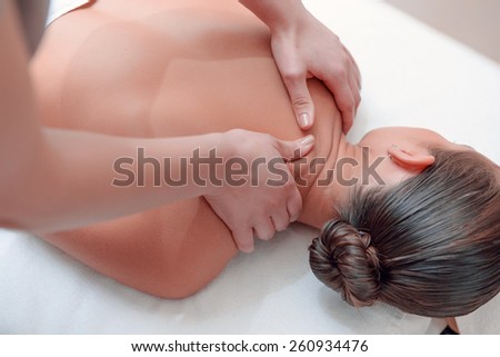 Massage for tired body. Beautiful young woman lying on front and keeping eyes closed while massage therapist massaging her back in spa