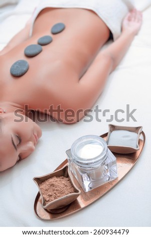 Stone SPA. Top view of young woman with shiny skin lying on front with spa stones on her back and massage treatment set