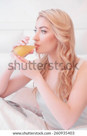 Good morning starts from breakfast in bed. Beautiful young woman drinking orange juice in bed and smiling