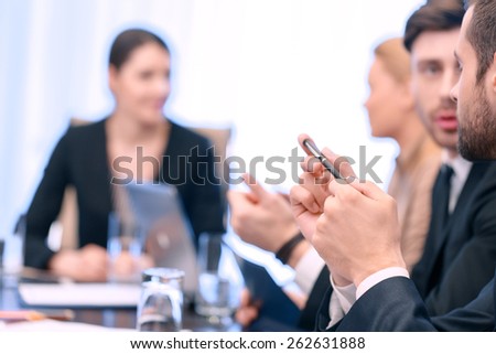 Small conversation at the meeting. Closeup of two male business partners communicating at the meeting with blurred background of other meeting participants