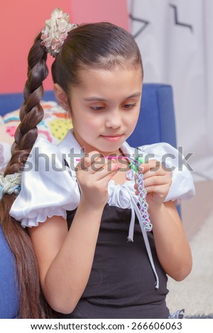 Creative job. Portrait of a small girl making a colorful rubber bracelet