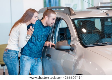 It is beautiful. Smiling young couple standing alongside a car and leaning against it watch at the interior of a new car
