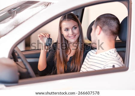Happy owners. View from the front door of the car on a young beautiful girl showing keys to her couple sitting next to her in the car