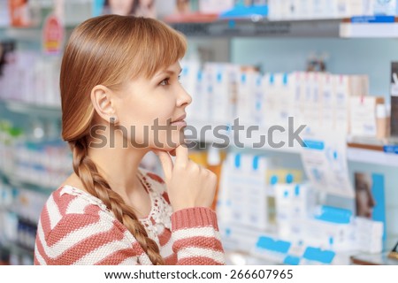 Wide range of beauty products. Young attractive woman looking at the shelves with medications at the pharmacy