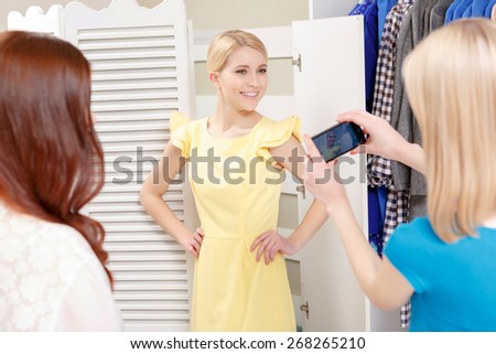 Pretty woman. Selective focus on a pretty young female shopper in a new dress being photographed by her friends in a fashionable boutique