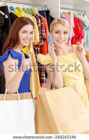 Best shopping. Two smiling women happily holding paper bags copyspace while one shows thumb up and the other speaks over the phone