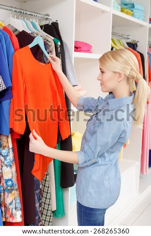 Shopping time. Joyful female shopper holding a hanger with a red blouse at clothing shop