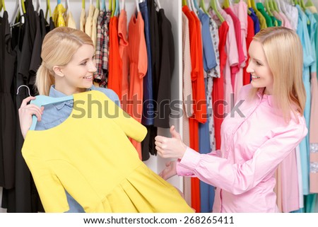 Perfect choice. Young woman trying a yellow dress and a salesman approves of her choice showing her thumb up