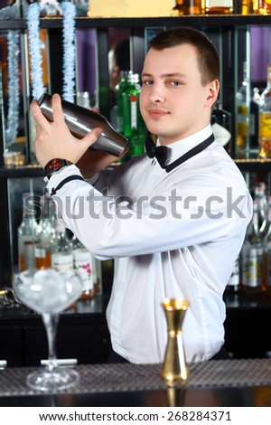 Barman job. Young handsome barman mixing cocktails in shaker at the bar