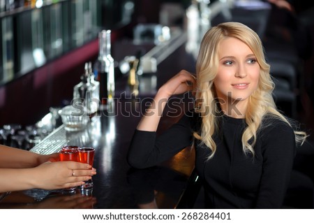 Nightclub. Portrait of a beautiful blonde girl sitting by the bar counter and having a drink