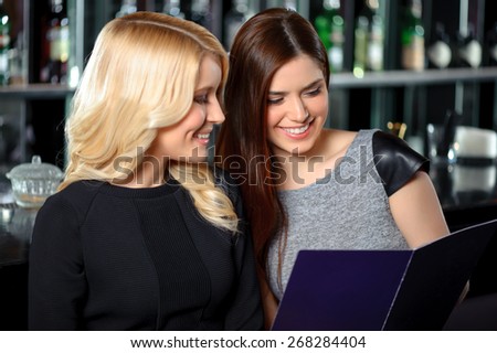 Ordering cocktails. Beautiful blond and brunette girls examining menu in the bar or nightclub