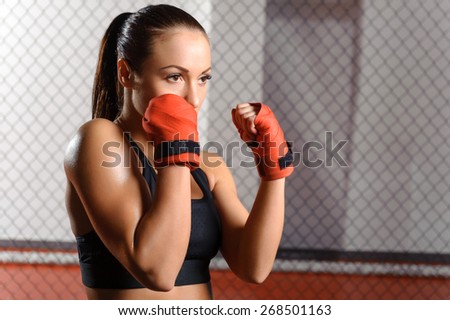 Professional fighter. Young beautiful woman in red boxing bandages ready to fight opponent in a boxing ring