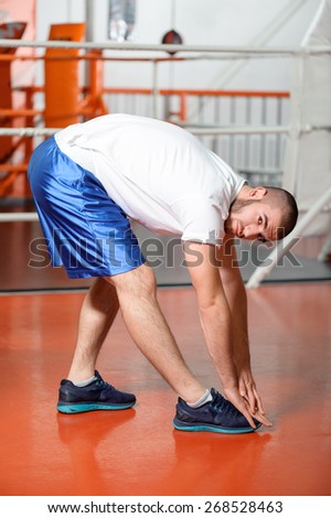 Professional sport. Young fit man stretching in a boxing ring and looks at a camera