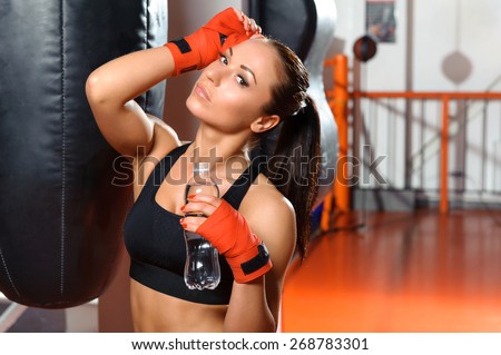 Small sip of water. Close-up of a seductive sportswoman holding a bottle with water in boxing gym