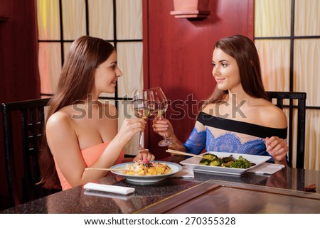 Cheers.  Two beautiful female friends toasting with wine in an oriental restaurant
