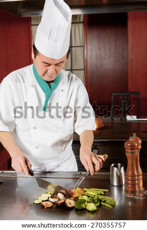 Oriental cuisine. Japanese cook making a dish out of fried mushrooms, broccoli, asparagus, sweet pepper and zucchini