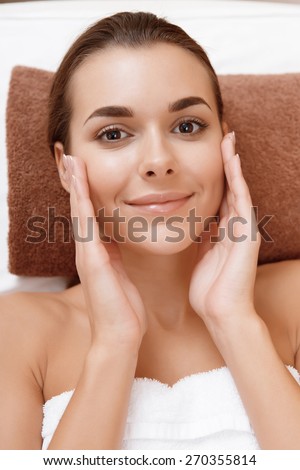 Divine softness. Close-up of a young attractive woman joyfully palming her face with a smile at beauty parlor
