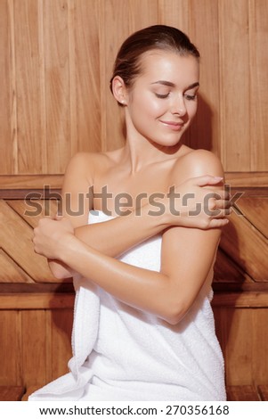 Beauty care. Vertical shot of a young joyful woman caring after her skin in wooden sauna room