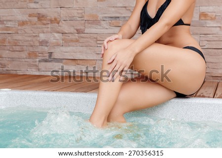 Soft skin. Cropped view of a young lady scrubbing her skin on legs near the Jacuzzi