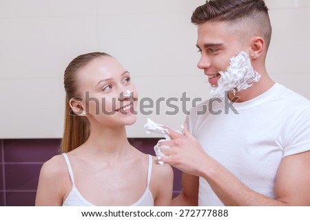 Have fun. Young man sharing his shaving gel with his girlfriend.