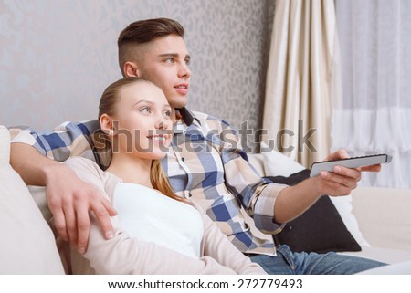 Channel-surf. Beautiful youthful man and woman sitting on white sofa and changing tv channels.