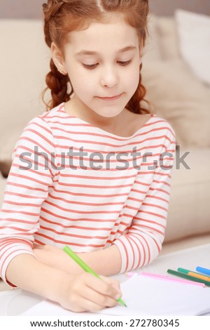 Learn to draw. Portrait of little concentrated girl sitting still and drawing with colorful crayons.