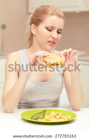 Unsatisfied with lunch. Young lady having lunch holding hamburger in her hands but having no desire to eat it