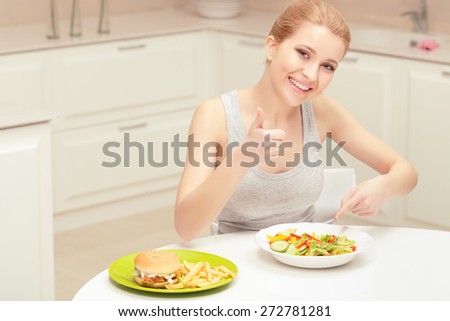 Thumb-up. Nice woman showing thumb-up and pointing on the plate with salad in order to show preferring healthy food to junk food