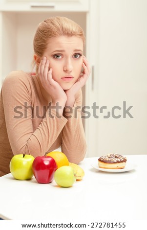 Hard to make right choice. Young lady holding face with her hands being depressed and in bad mood because of difficulties of choosing between healthy and tasty food