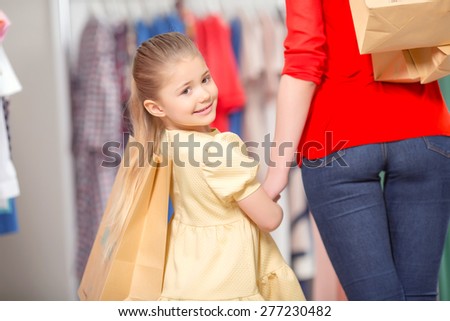 Portrait of a small girl standing in a fashion store holding the hand of her mother and packages