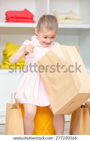 Look inside. Small happy girl looking inside her package with a new dress in a fashion store