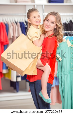 Shopping. Young mother standing in a fashion store holding her daughter with packages both smiling