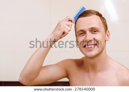 Styling hair. Handsome topless man brushing his hair with help of little comb