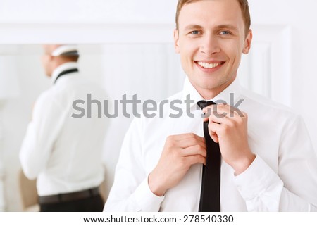 Finishing touches. Young smiling man fixing his tie on background of mirror.