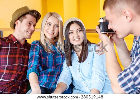 Young boy making a photo of his friends sitting and smiling in a yellow room using a vintage camera selective focus