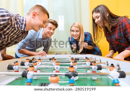 Boys vs girls. Young smiling boy playing air hockey against young Asian girl watching the play while their friends standing near and cheering them up