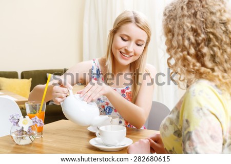 Taking care. Beautiful blond woman pouring out cup of tea in cafe.
