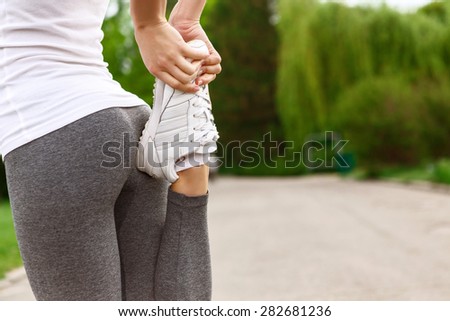 Stretch out. Close up of young woman doing stretching exercises by pushing her leg to ass