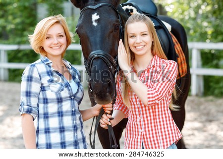 Want to ride. Smiling sisters having enlightened mood while standing near the horse and caressing it.