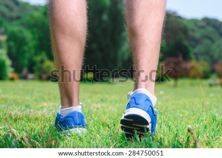 Picture of muscled legs of a sportsman running on a green grass wearing blue sneakers during training in the park, close up