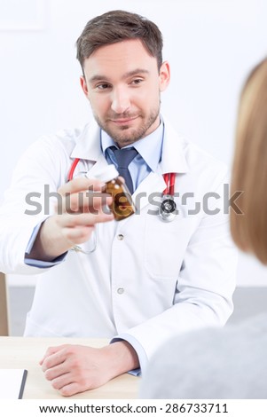 Take it. Pleasant cardiologist giving medicines to the patient and looking at her while examining her.