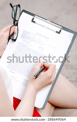Close up photo of a professional female psychologist wearing white blouse red skirt, sitting in the armchair and making notes on her clipboard in her office during therapy session
